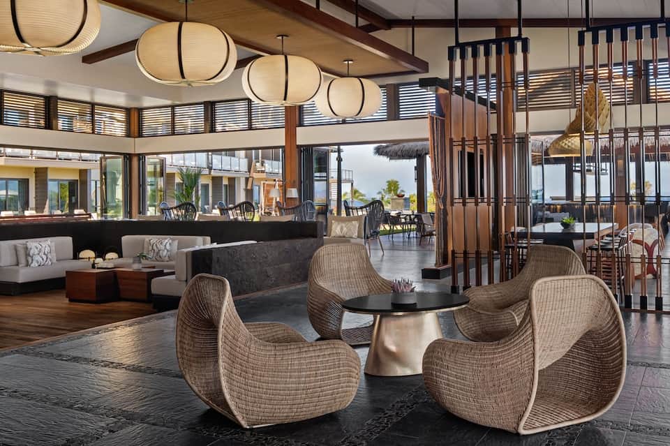 Modern hotel lobby lounge with pendant lighting, woven chairs, and ocean view through glass doors