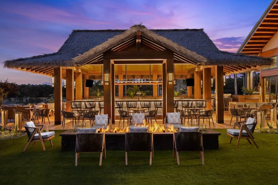 Luxury outdoor pavilion with thatched roof, fire pit, and lounge seating at dusk