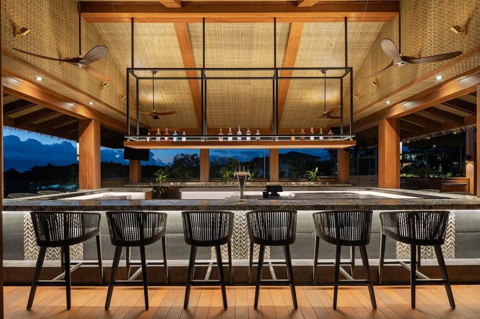 Upscale outdoor bar with wooden beams, woven ceiling panels, and illuminated beverage display