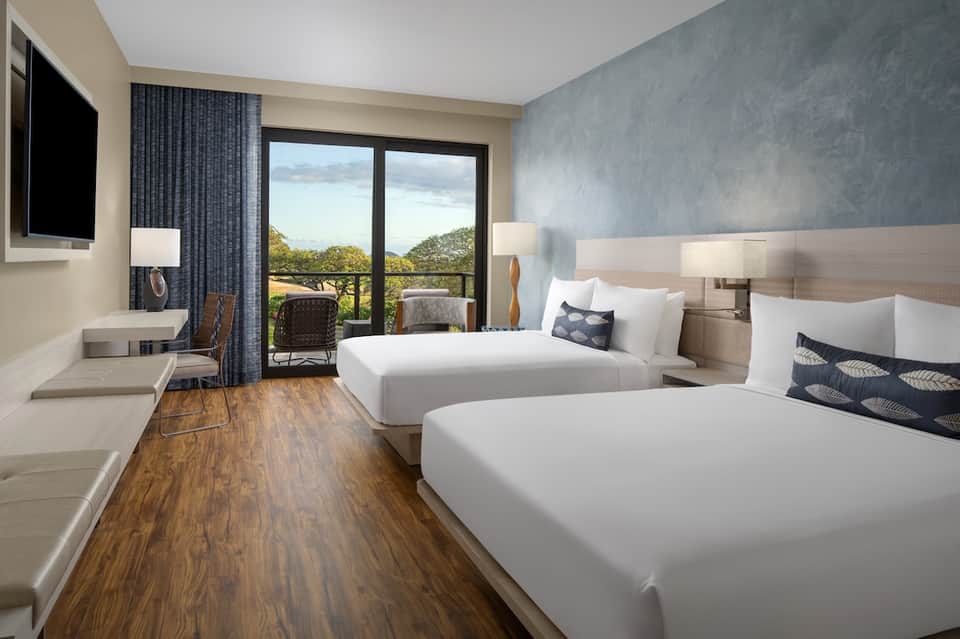 Hotel room with two queen beds, wooden flooring, balcony doors, and nature landscape views