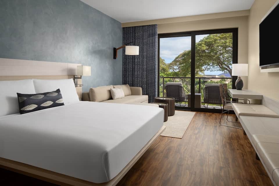 Hotel bedroom with queen bed, blue accent wall, balcony doors, and nature views