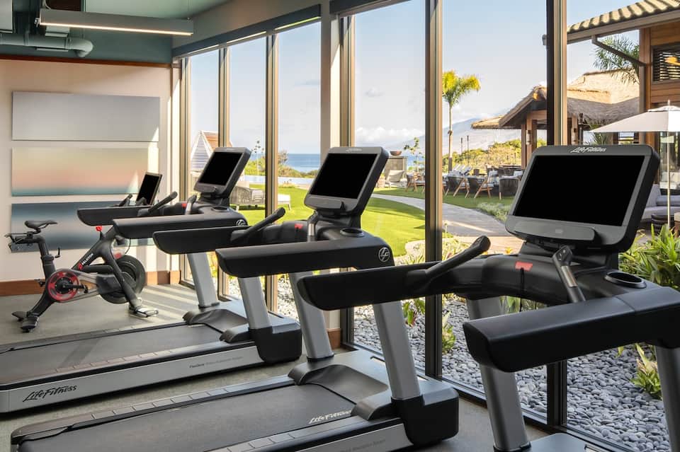 Luxury fitness facility with stationary bikes and treadmills overlooking ocean and tropical landscape