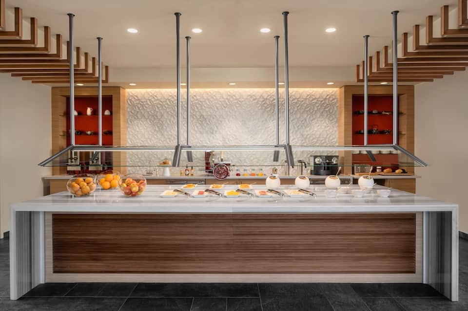 Upscale hotel buffet counter with white marble top, wood accents, and fresh fruit displays