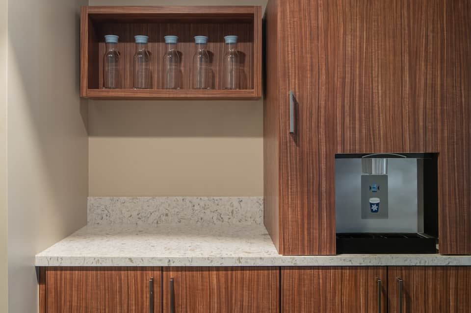 Mini bar station with wooden cabinetry, marble countertop, water bottles in glass display, and ice dispenser