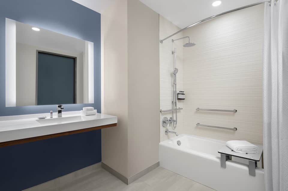 Modern bathroom with illuminated mirror, dark vanity, white tile, and walk-in shower area