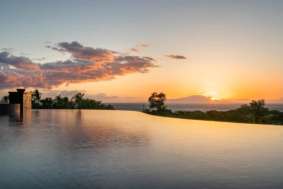 Infinity pool overlooking ocean at golden sunset with palm trees and architectural elements