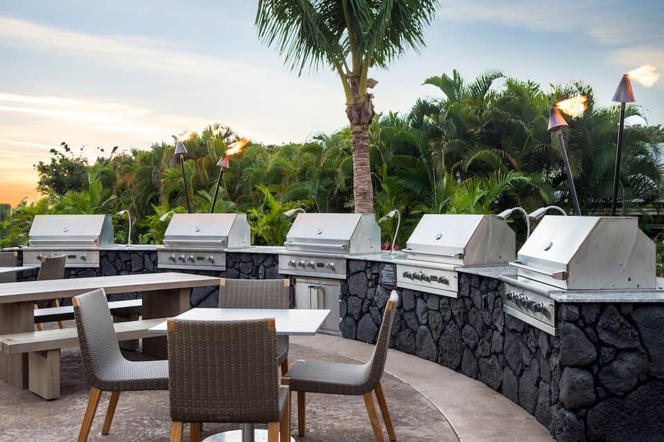 Outdoor grill station with multiple built-in barbecues overlooking tropical gardens at sunset