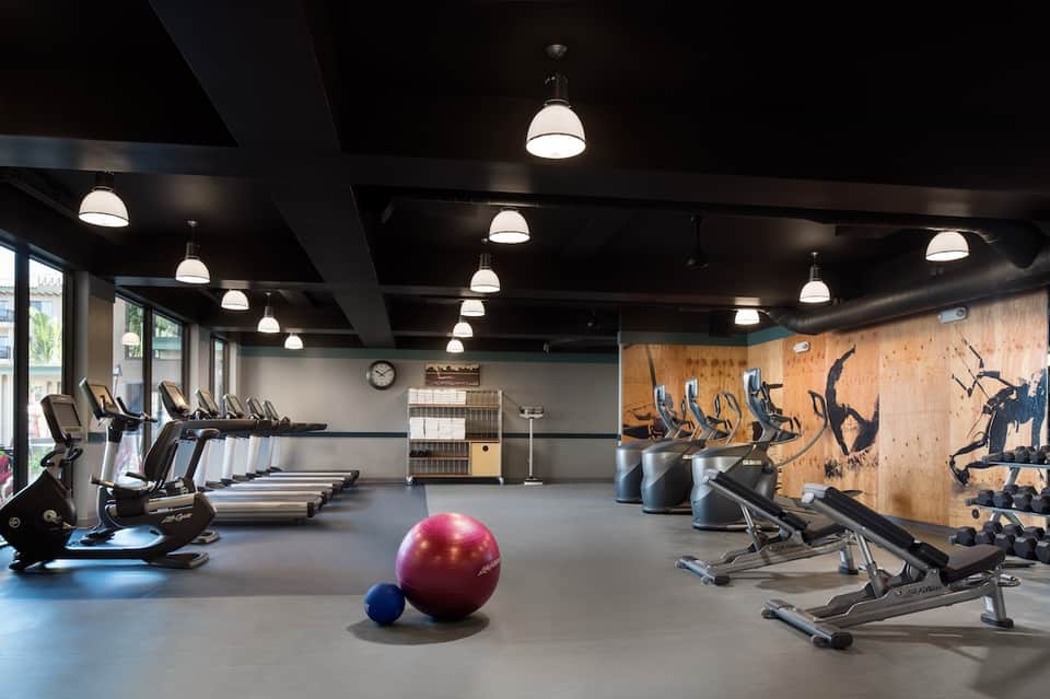 Spacious gym with exercise bikes, treadmills, wooden accent wall, and purple exercise ball