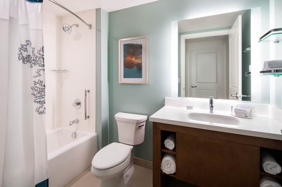Guest bathroom with seafoam walls, white vanity, dark wood cabinets, and rainfall shower