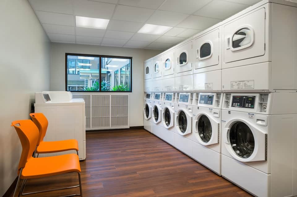 Hotel laundry facility with rows of white washing machines and dryers, orange accent chair