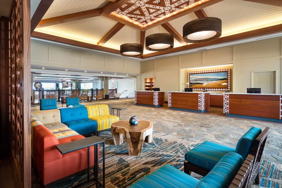Hotel lobby with colorful seating, wooden ceiling beams, reception desk, and geometric wall patterns