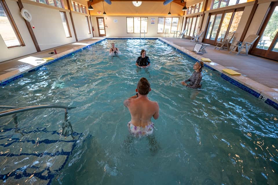 Indoor swimming pool with people in water, wooden ceiling beams, and bright natural lighting