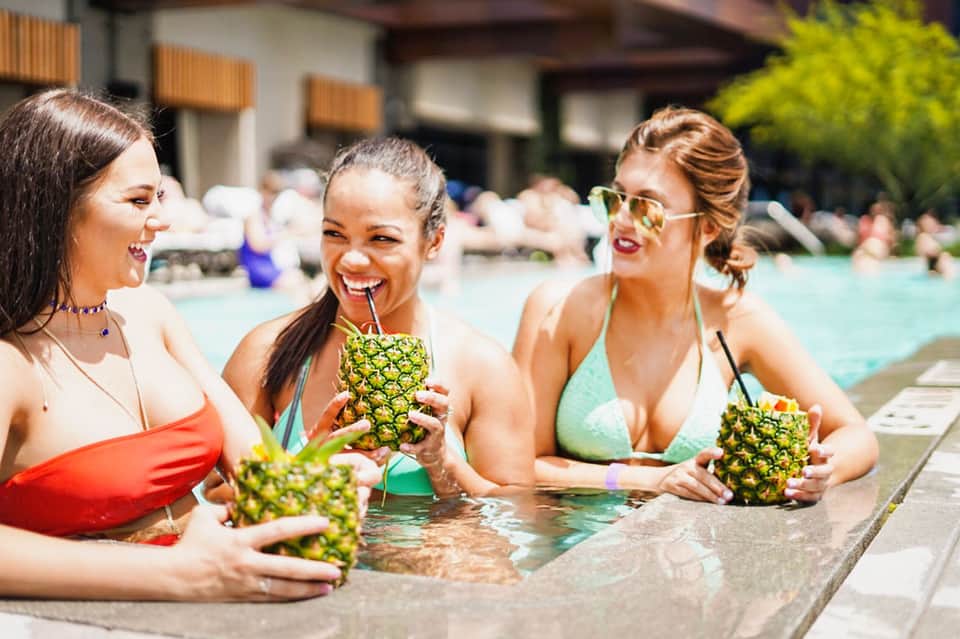 Three women in pool holding tropical pineapple drinks