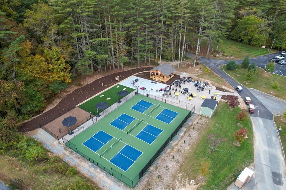 Aerial view of pickleball courts with green playing surfaces surrounded by forest
