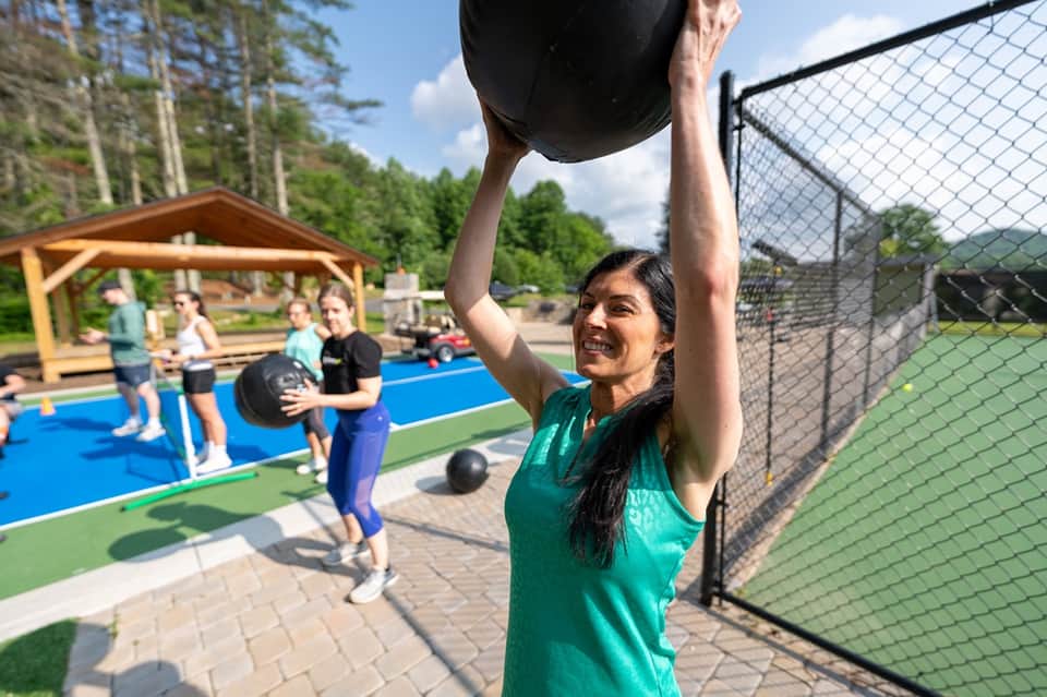 Woman doing fitness training outdoors with medicine ball near sports court and pavilion