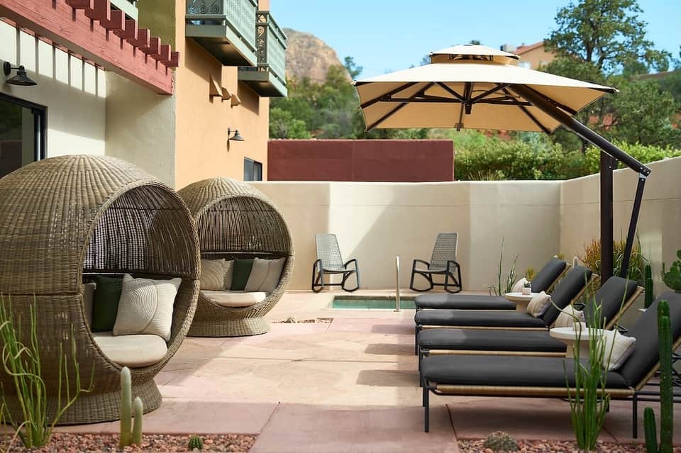 Resort patio with woven egg chairs, loungers, cantilever umbrella, small pool, and scenic mountain backdrop