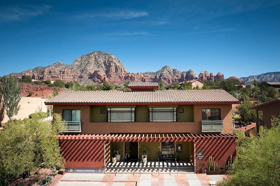 Two-story southwestern home with terracotta exterior, red tile roof, striped awning, and red rock formations backdrop