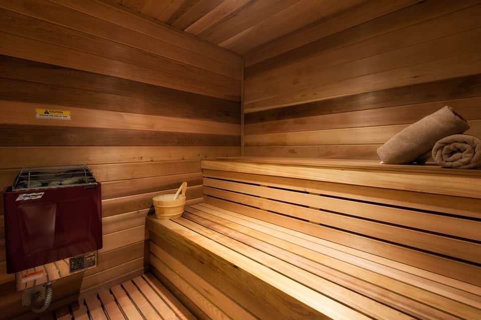 Wooden sauna interior with tiered benches, rolled towel, wooden ladle, and heater equipment
