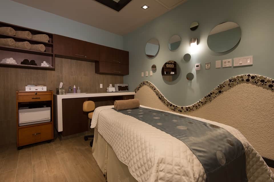 Spa treatment room with mint green walls, circular mirrors, textured headboard, and massage bed