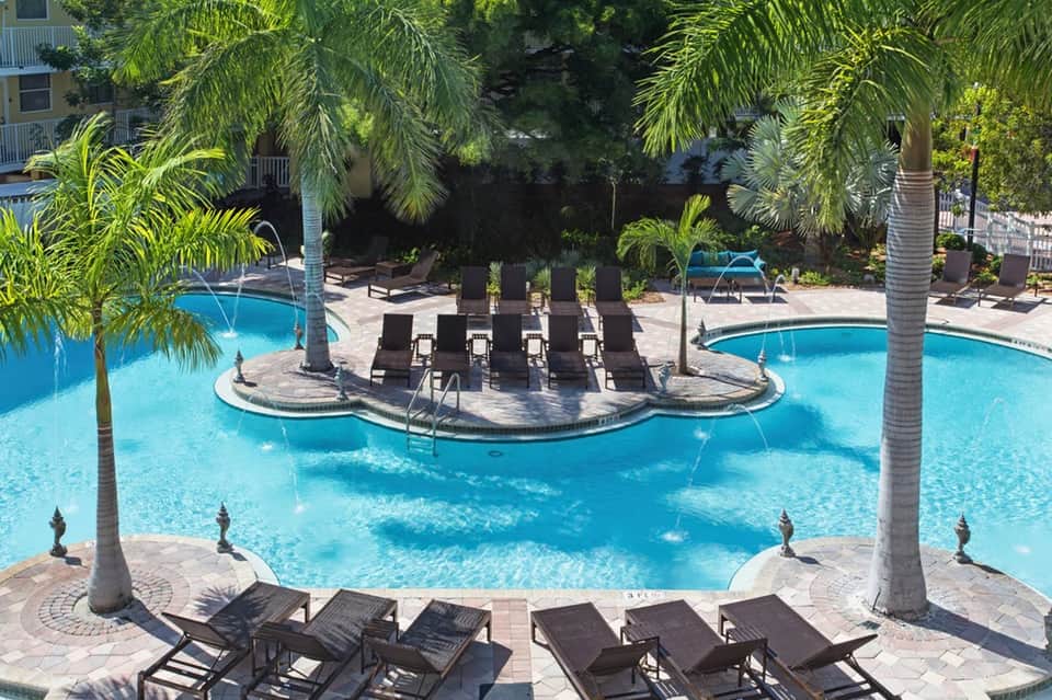 Resort pool with island cabanas, palm trees, lounge chairs, and surrounding landscaping