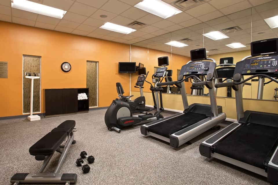 Fitness center with orange walls, treadmills, exercise bikes, dumbbells, and cardio equipment