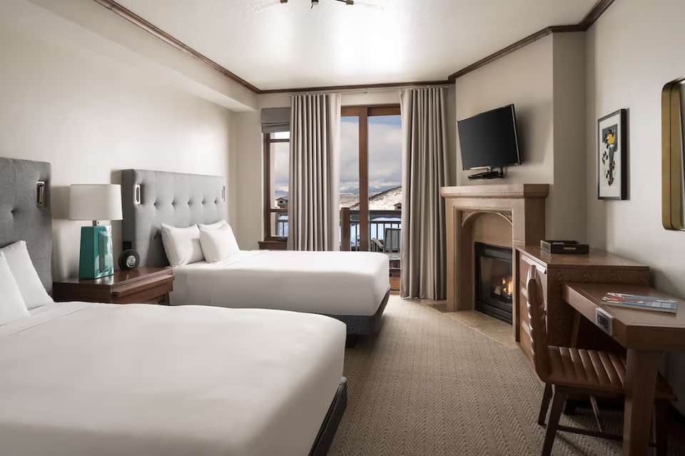 Upscale hotel room with two queen beds, fireplace, balcony with scenic mountain views, neutral decor
