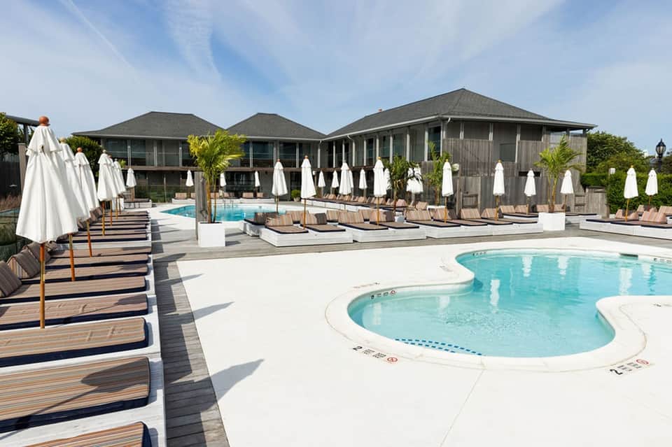 Outdoor pool area with white umbrellas, wooden lounge chairs, and modern building structure