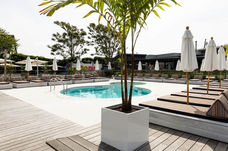 Rectangular swimming pool surrounded by white umbrellas, loungers, and landscaped grounds
