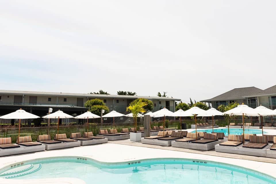 Resort pool deck with white umbrellas, striped lounge chairs, and calm turquoise water
