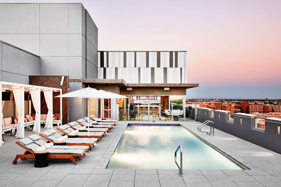 Rooftop pool deck at sunset with loungers, umbrellas, and modern urban skyline views