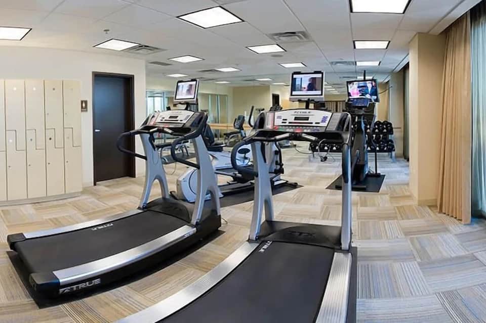 Compact hotel fitness room with treadmills, exercise bikes, and overhead lighting