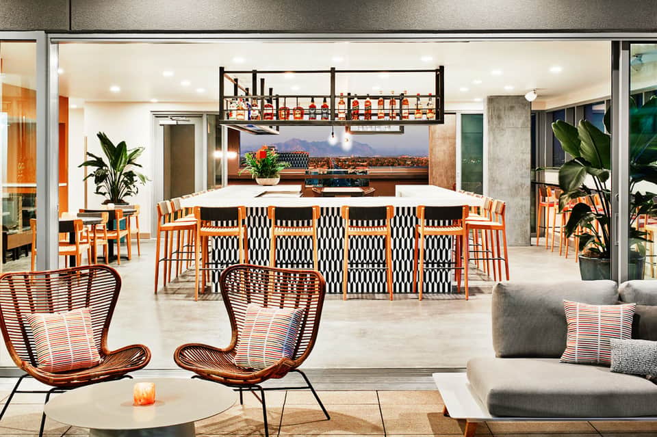Modern resort bar and lounge with orange accents, high ceilings, mountain views, and contemporary furnishings