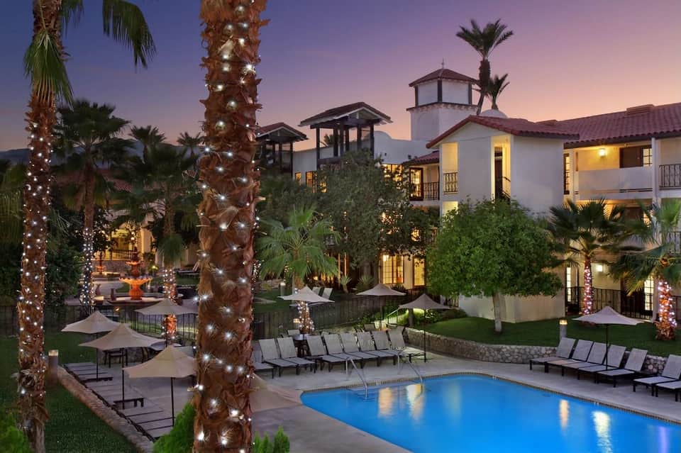 Luxury resort courtyard at dusk with illuminated palms, pool, and architecture