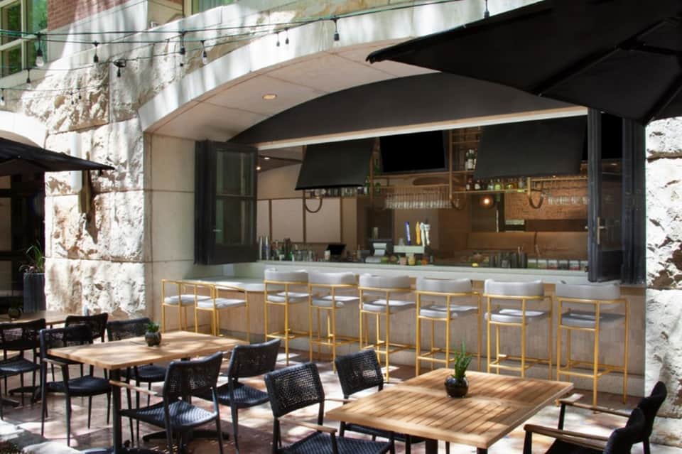 Modern outdoor bar and dining patio with wooden counter, bar seating, and stone architectural elements