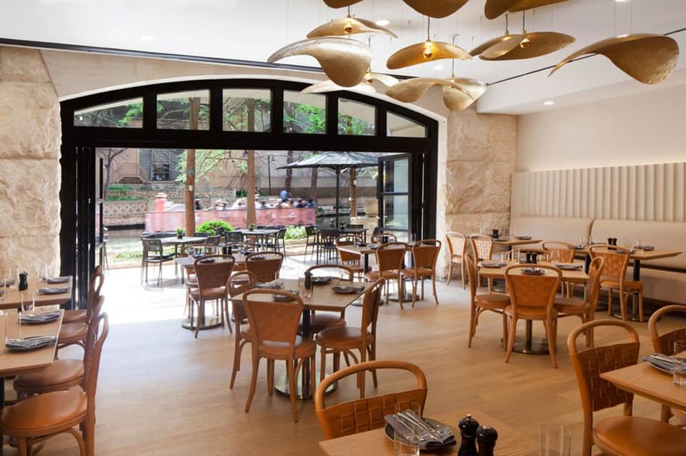 Restaurant dining area with wooden chairs, brass pendant lights, and outdoor patio access