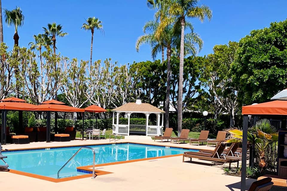 Resort pool surrounded by palm trees, orange umbrellas, lounge chairs, and white gazebo