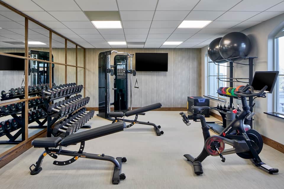 Modern gym with dumbbells, exercise bike, weight machines, and mirrored walls