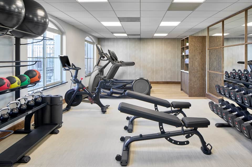 Fitness gym with exercise equipment, dumbbells, stationary bike, natural light, and modern interior design