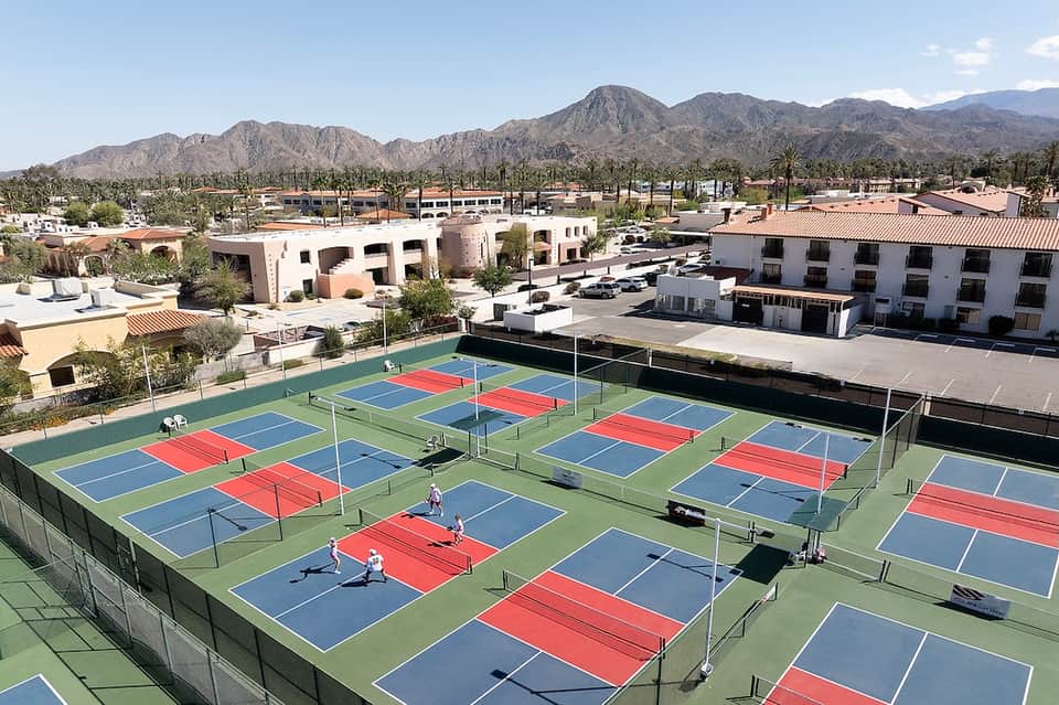 Multiple tennis courts with blue and red playing surfaces in desert setting