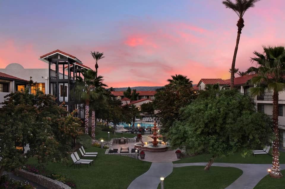 Resort grounds at sunset with palm trees, manicured lawn, and illuminated pathways