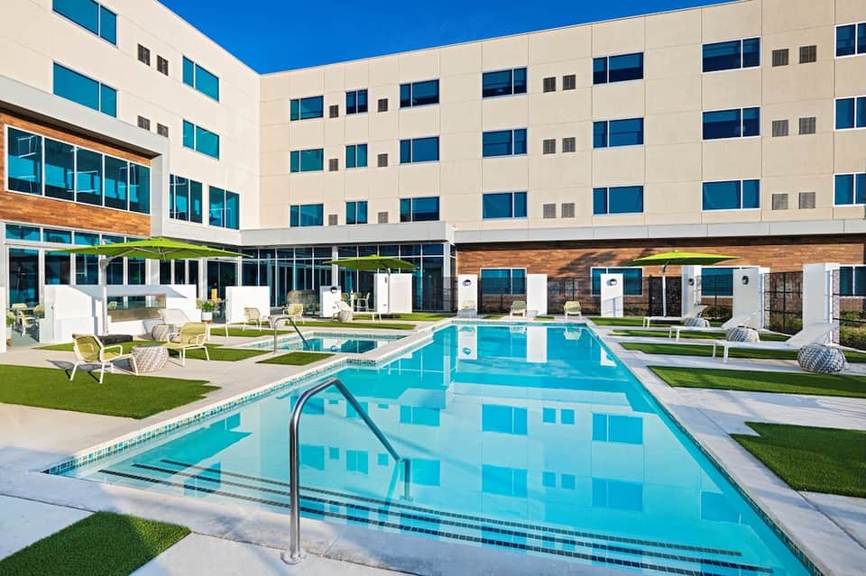 Resort pool deck with white loungers, green umbrellas, and modern building