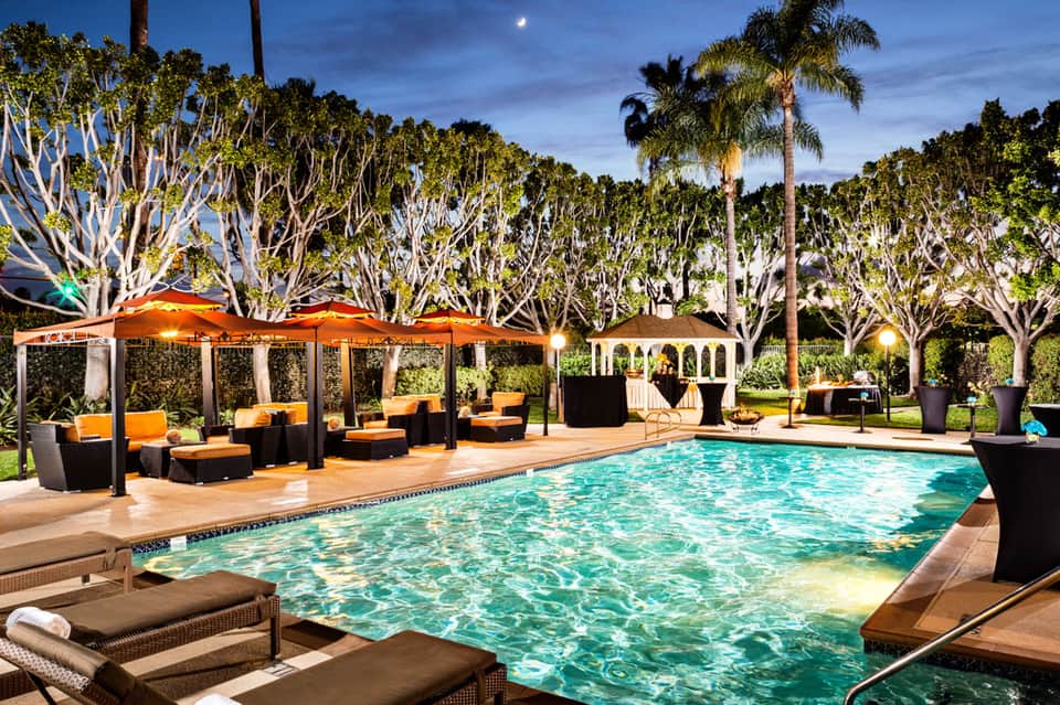 Twilight poolside lounge with orange umbrellas, palm trees, and comfortable seating