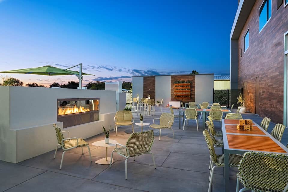 Modern rooftop patio at dusk with fireplace, dining tables, and shade structures against twilight sky