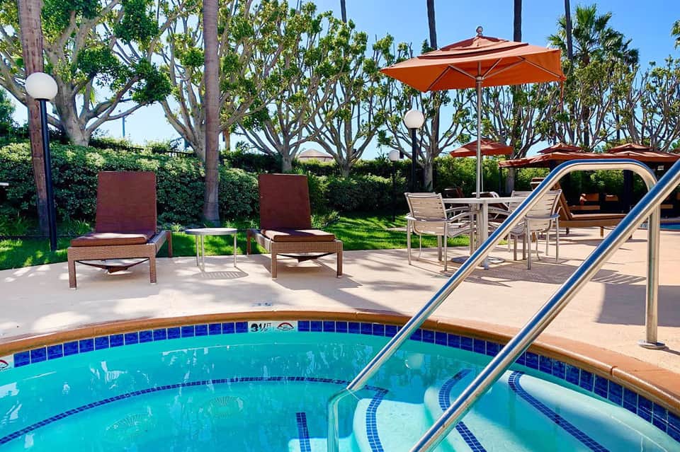 Resort pool with palm trees, lounge chairs, and orange umbrellas