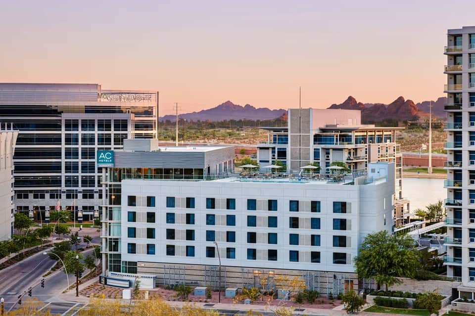Modern white hotel building with rooftop pool against desert mountain backdrop