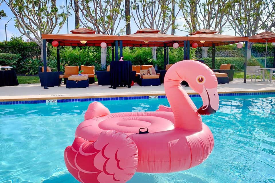 Resort pool with pink flamingo float, lounge seating, and red umbrellas under palm trees