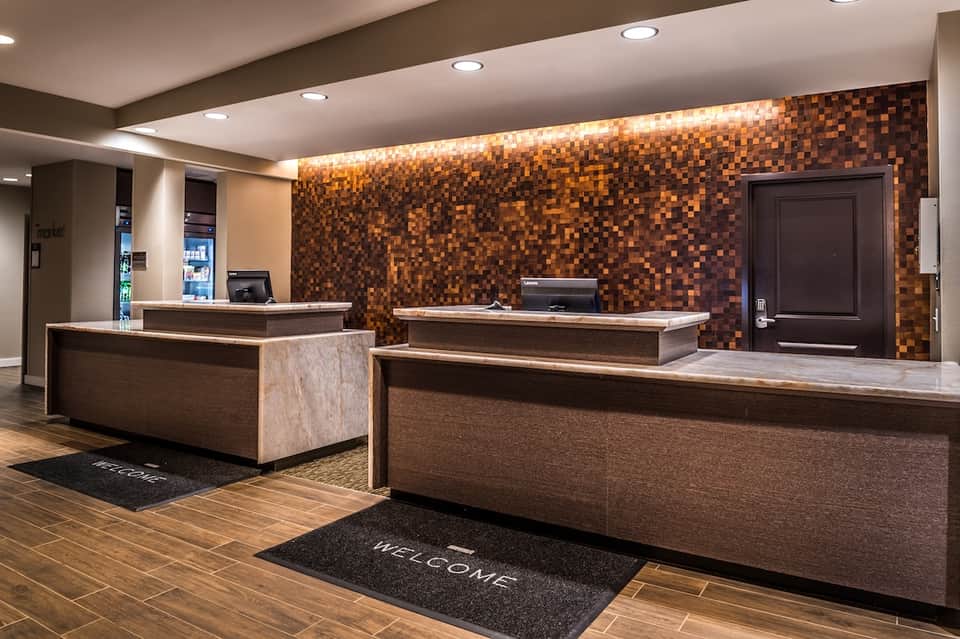 Hotel lobby with copper tile accent wall, two reception desks, and welcome entrance mat