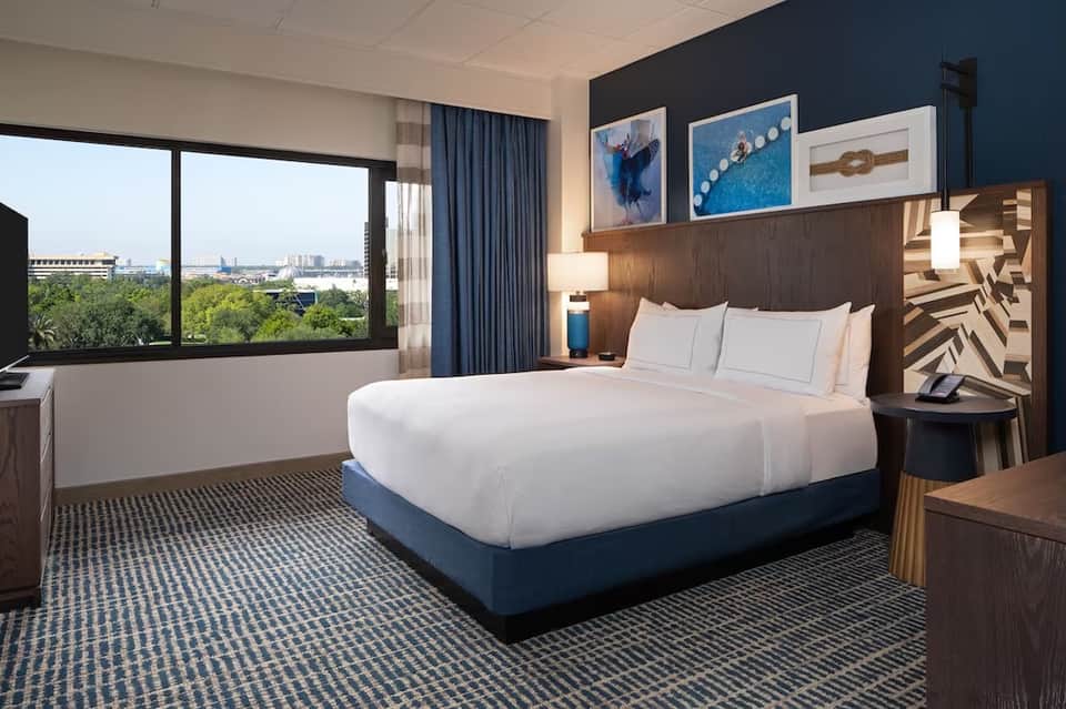 Modern hotel bedroom with king bed, city view, blue accent wall, and contemporary furnishings