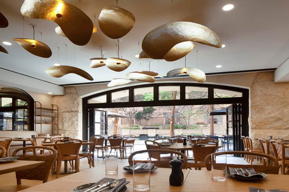 Modern restaurant interior with suspended brass light fixtures and outdoor courtyard