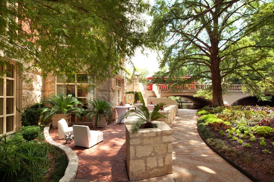 Mediterranean-style courtyard with stone architecture, tropical plants, and shaded seating areas